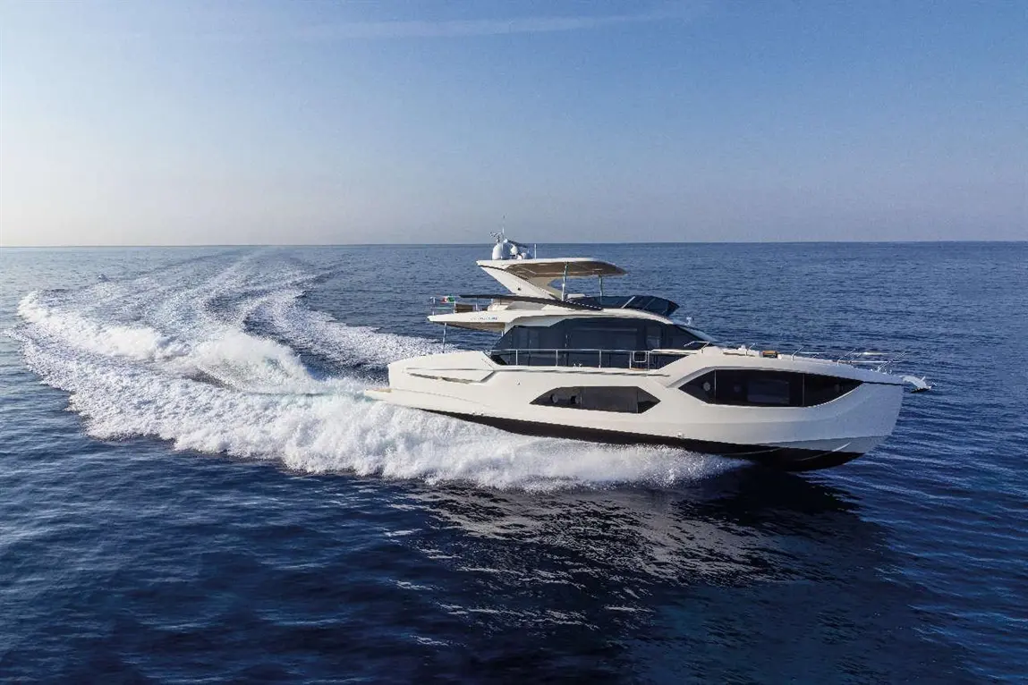 A sleek luxury yacht moves swiftly across calm blue waters, leaving a wake beneath a clear sky.
